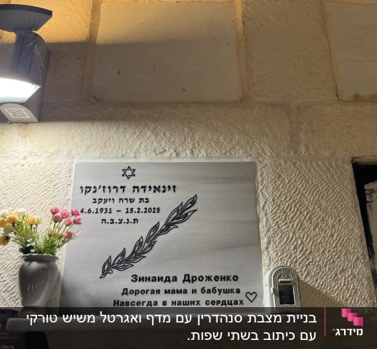 מצבה עם כיתוב בעברית ורוסית, פרחים ונר זיכרון